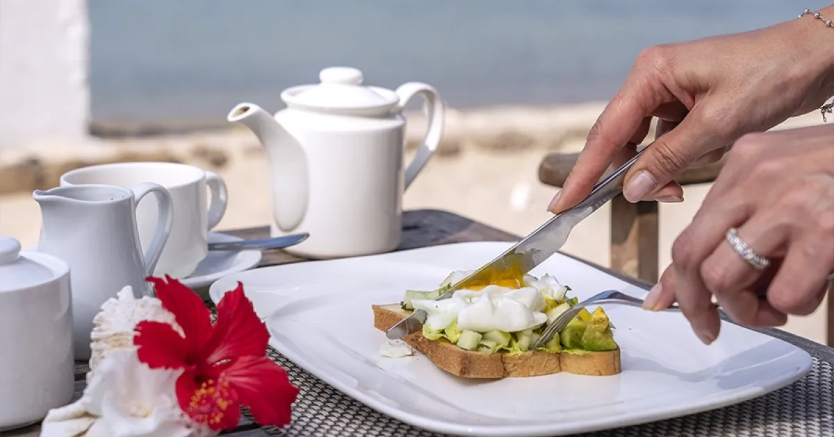 Colazione proteica vista mare con toast, avocado e uovo, un'idea per le vacanze estive.