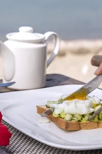 Colazione proteica vista mare con toast, avocado e uovo, un'idea per le vacanze estive.