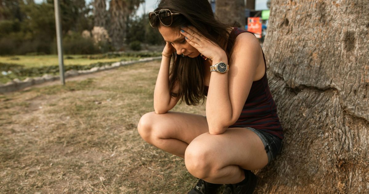 ragazza al parco con aria stressata appoggiata a un albero