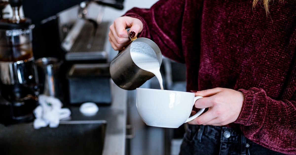 foto di una ragazza con un maglione che versa del latte da un bricco in una tazza per cappuccino, in cucina. foto per articolo su latte proteico