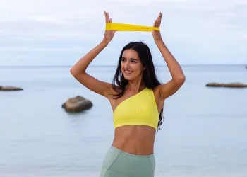 Sportiva sorridente che esegue un esercizio con un elastico in spiaggia, un'idea di workout per la routine estiva GFF.