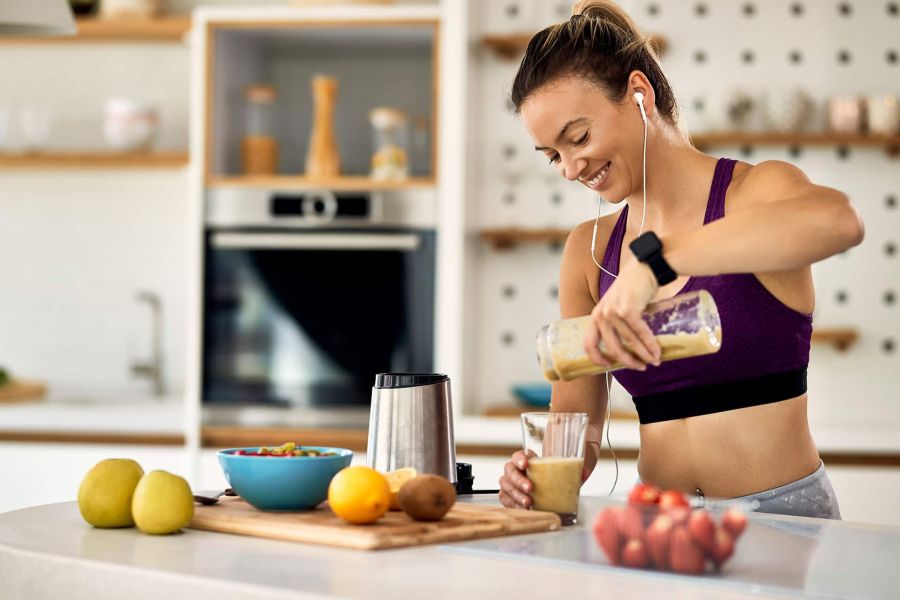 Assunzione di proteine prima dell’allenamento: donna prepara uno shaker proteico in cucina.