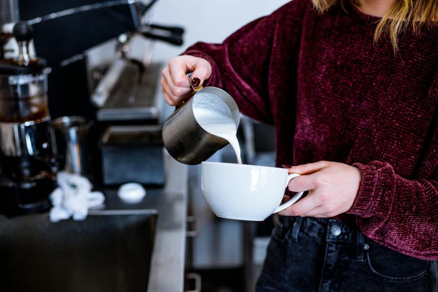 foto di una ragazza con un maglione che versa del latte da un bricco in una tazza per cappuccino, in cucina. foto per articolo su latte proteico
