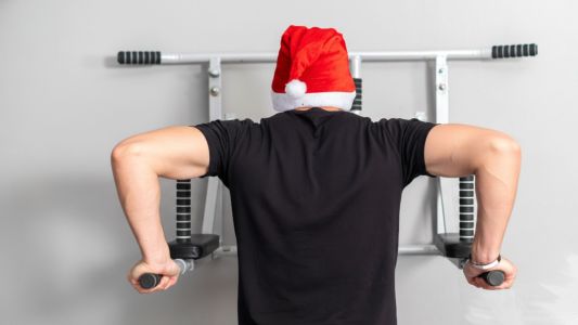 Uomo di spalle che esegue dei dips alle parallele indossando un cappello di Babbo Natale in palestra