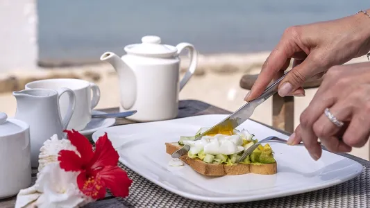 Colazione proteica vista mare con toast, avocado e uovo, un'idea per le vacanze estive.