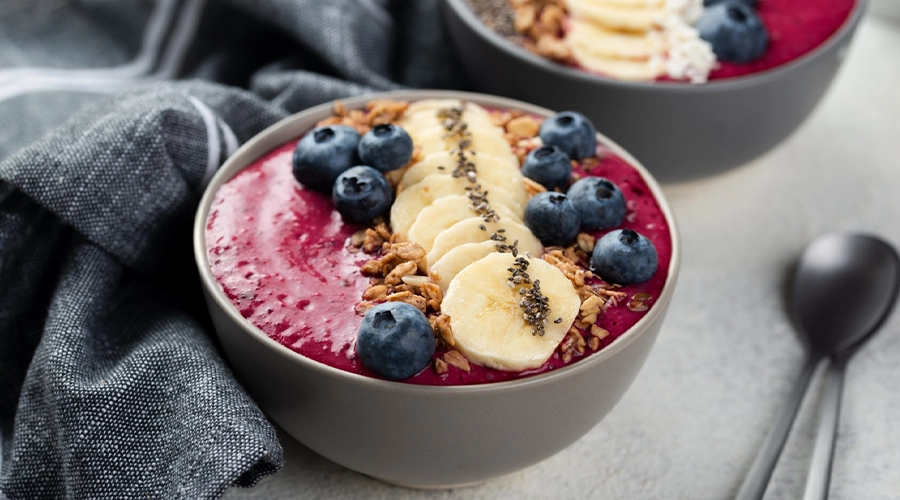 Bowl di smoothie proteico estivo guarnita con mirtilli, banana e granola, un pasto fresco e nutriente.