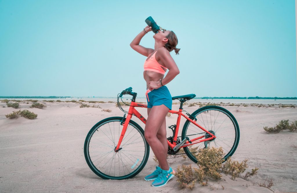 donna che beve da una borraccia in estate mentre va in bici sulla spiaggia